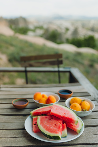 Front view of fresh fruits with tea on the wooden table on patio with scenic view of beautiful rock formations in Nevsehir province, Middle East