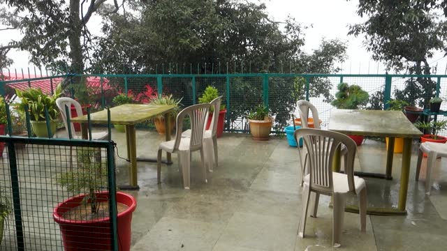 An image of an outdoor garden balcony with empty chairs and a table during a rainy monsoon season in Himachal Pradesh, India