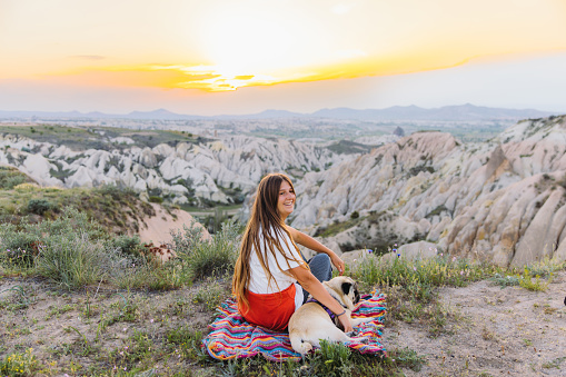 Rear view of female with long hair and a pug admiring the sunset with a view of the beautiful valley Göreme National park, Middle East
