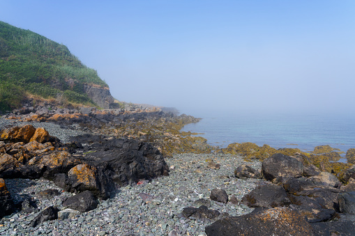 A foggy summer afternoon on the rock strewn foreshore beneath the cliffs of Porthdinllaen bay in Wales.