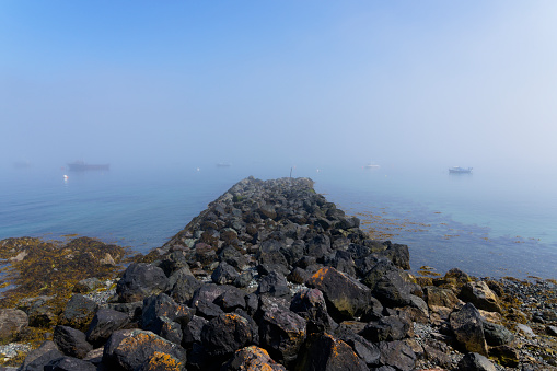 A small jetty built from rocks pokes out into a fog shrouded Porthdinllaen bay in Wales.