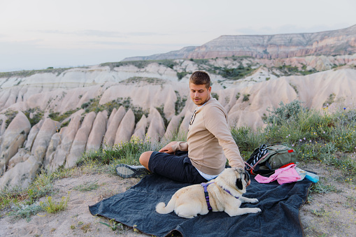 Side view of happy male admiring the sunset with their pug, with a view of the beautiful valley in Göreme National park, Middle East