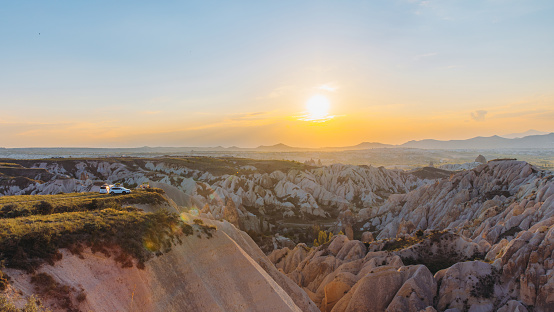 High-angle panoramic view of unusual rocky colourful landscape in the mountains at Goreme, Middle East during bright pink-yellow sunset with background view of mountain peaks