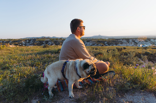 Side view of happy male admiring the sunset with their pug, with a view of the beautiful valley in Göreme National park, Middle East