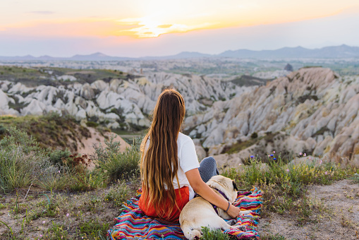 Rear view of female with long hair and a pug admiring the sunset with a view of the beautiful valley Göreme National park, Middle East