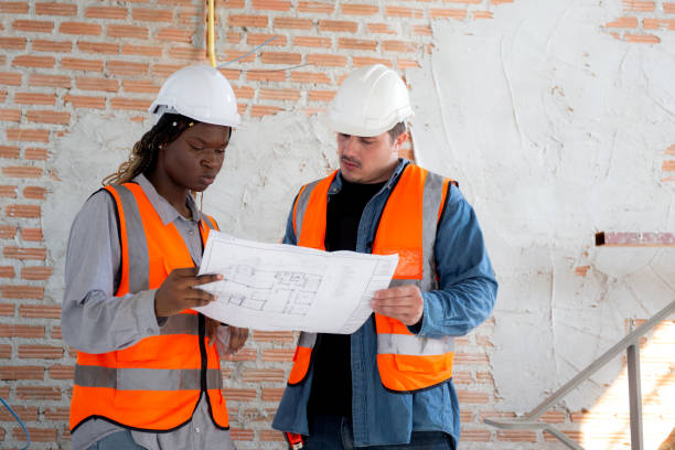 Team of architect or engineer wearing hardhat looking blueprint for inspection and planning construction at construction site, contractor or builder examining and checking project development house. stock photo