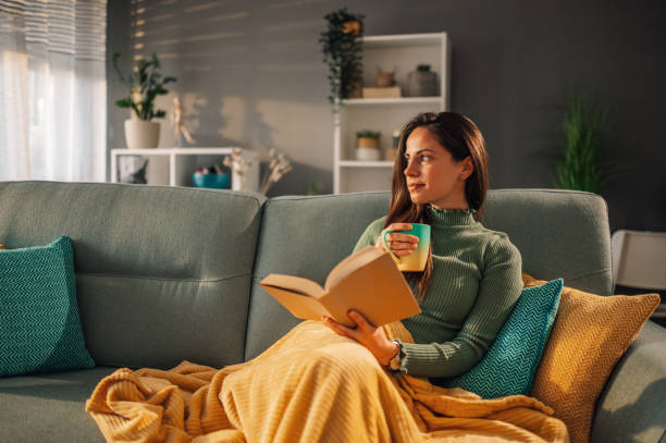istock Woman sitting on comfy couch reading a book and drinking coffee or tea 1937328314