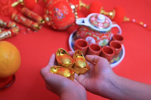The hands of a teenage girl holding a golden ingot with items decorated on the Chinese New Year concept against a red background.  Chinese letter means Rich and lucky