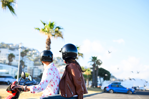 Mature couple riding scooter on tropical beach front with apartment blocks and golden sunlight