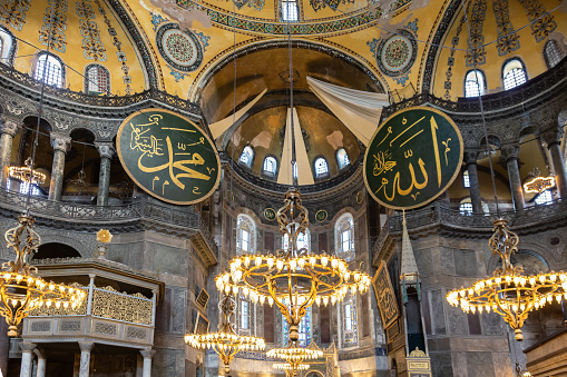 Hagia Sophia interior. Part of the central nave and concha with gold mosaics clothed with textile. Panels with text from Q'ran on either corner. May 10, 2022. Istanbul, Turkey