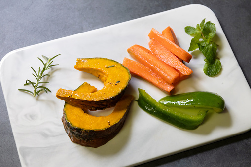 Pumpkin, carrot and bell pepper sliced with rosemary and pepper on a marble plate.