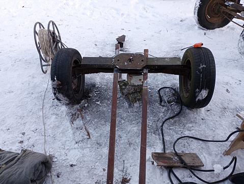 Wheelbase of a car with two wheels on the street in winter for conversion to a trailer. An electric extension cord and a hand tool are nearby.