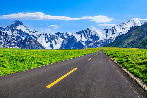 Asphalt highway and green meadows with snow mountain natural landscape under the blue sky