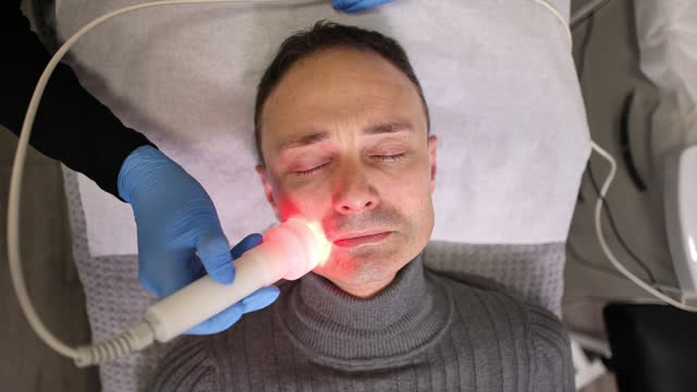 Close-up of an mid-adult man receiving an led therapy facial treatment from a female Caucasian beautician