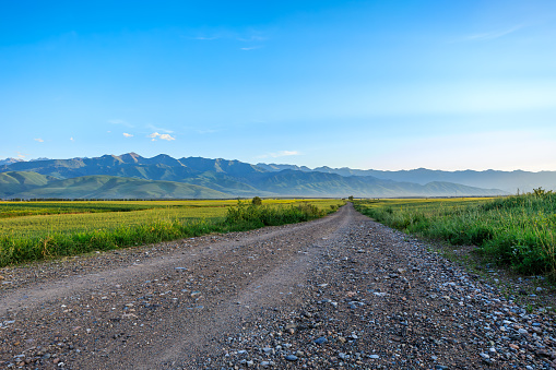 Country gravel road and green farmland with mountain natural landscape under blue sky