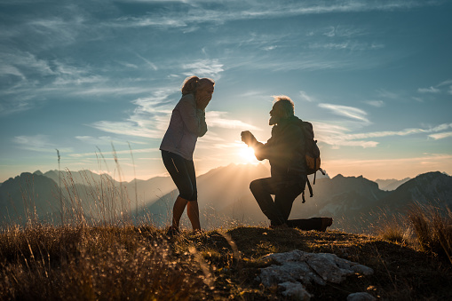 In a mountainous setting, a mature couple celebrates love and happiness, highlighted by a surprise engagement proposal carefully arranged by the man.
