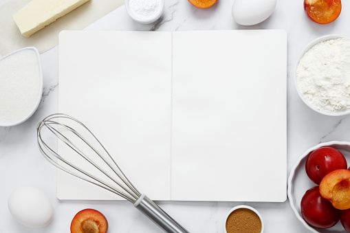 Ingredients for making classic cake pie with plums on white background. Concept homemade food, seasonal pastries. Mock up notebook. Top view, copy space