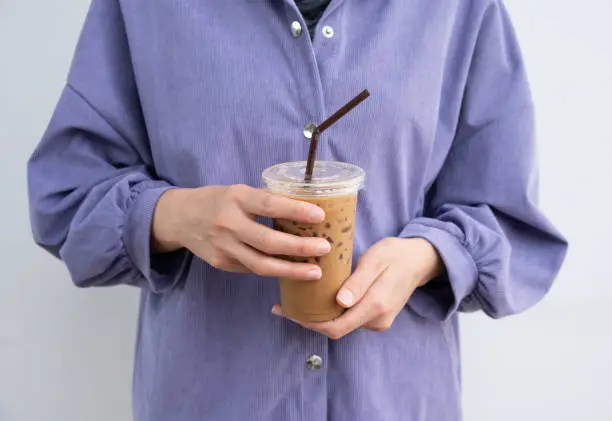 Photo of Cropped shot view of woman hand holding a plastic cup of iced milk coffee.