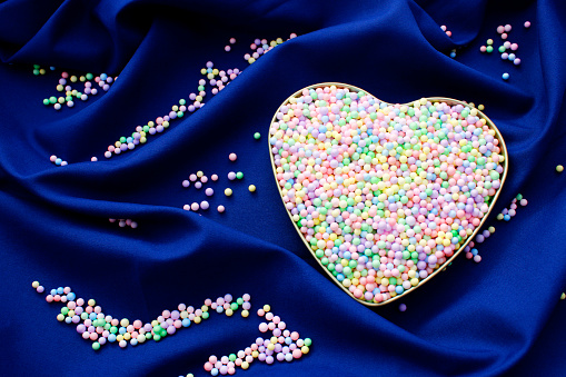 Heart filled with small spheres of different colors on blue background