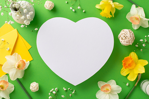 Welcome spring's awakening with narcissus and gypsophila. Top-view image captures fresh flowers and decorations on a green isolated background, heart-shaped frame ready for text or advertising