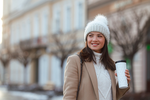 In the chill of winter, a woman strolls down a city street. She's carrying a bag filled with food and a reusable coffee cup. Wrapped up in a cozy white sweater, a beige coat, and topped with a white winter cap, she moves through the cool air with ease.
