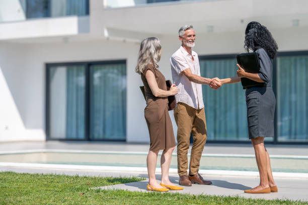 Real estate agent and couple handshake Female real estate agent showing luxury house to senior couple and shaking hands wide shot african american architecture stock pictures, royalty-free photos & images