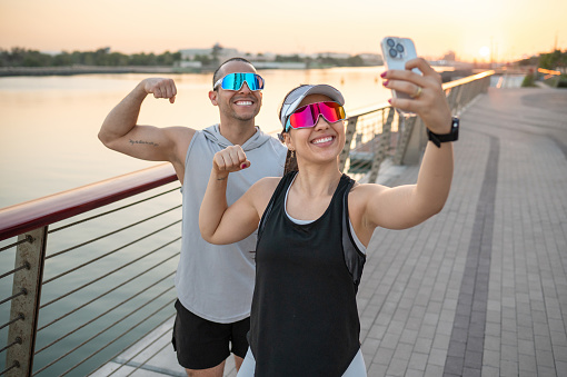 Active couple flexing muscles and capturing a selfie outdoors after successful daily training