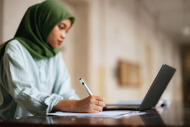 istock Anonymous Young Female Wearing Hijab Writing and Using Laptop Computer for Studying 1937529597