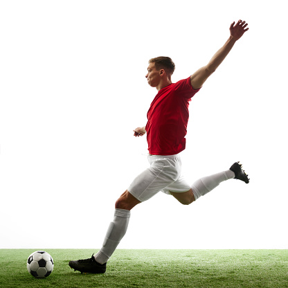 Goal bound elegance. Grace and power of a professional footballer mid-air passes to goal against white background with green grass. Concept of sport games, hobby, energy, world cup, match, movement.