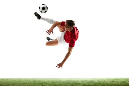 Dynamic airborne play. Dynamic soccer player kicks ball into air, showcasing unmatched skill against white background with green lush field. Concept of sport games, hobby, energy, movement. Ad
