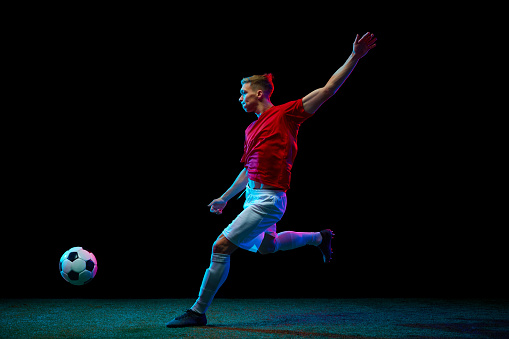 Precision in Motion. skilled football player delivers perfect airborne pass, showcasing unparalleled precision against black background in neon light. Concept of sport games, world cup season, match.