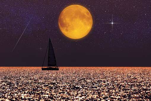Full Moon and Milky way rising above ocean sea horizon with sailing boat silhouette.