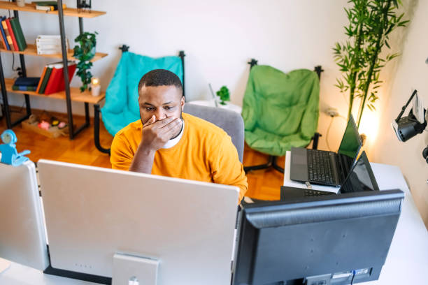 istock Young black man programmer sitting in front of computer screens and working as a freelancer at home settings. Looking worried. 1937556300