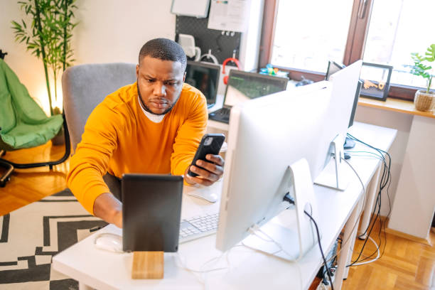istock Programmer sitting in front of computer screens and working as a freelancer at home settings. Looking at mobile phone. 1937556860