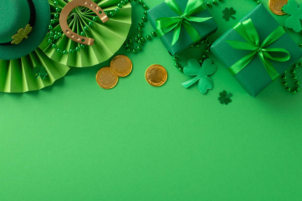 istock Festive St. Paddy's setup: Overhead shot featuring Irish charm. Leprechaun's hat, gift boxes, horseshoe, gold coins, fans, shamrocks, beads on green backdrop. Ad space available 1937582083