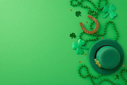 St. Patrick's Day celebration in a frame: Top view leprechaun's hat, horseshoe, shamrocks, confetti, beads arranged on a green surface. Customizable space for your message