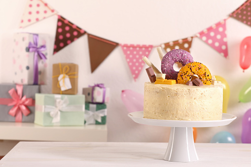 Delicious cake decorated with sweets on white wooden table in festive room, space for text