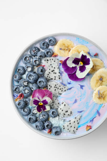 Delicious smoothie bowl with fresh fruits, blueberries and flowers on white background, top view