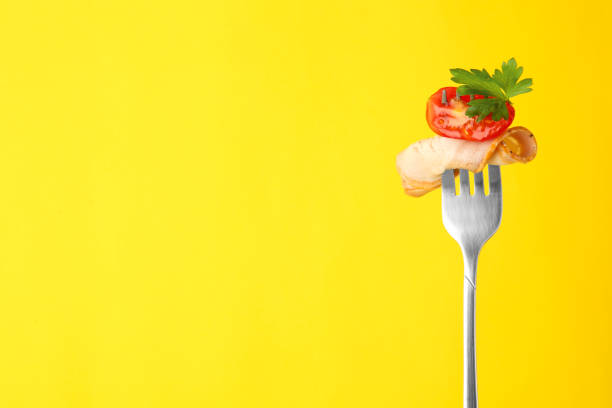 istock Fork with slice of ham, cut tomato and parsley on yellow background, space for text 1937612444