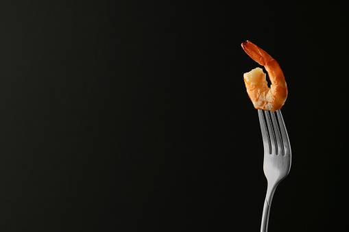 Fork with one shrimp on black background. Space for text
