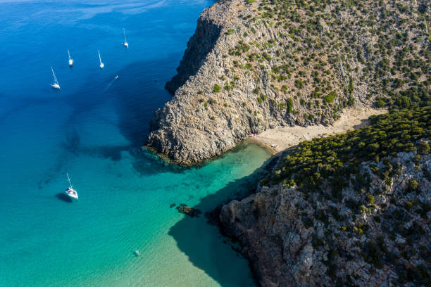 高い崖がイタリアのサルデーニャ島西部のカーラ・ドメスティカ湾を囲んでいます。サルデーニャ島は地中海で2番目に大きい島です。パラディースに停泊する帆船