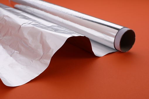 Roll of aluminum foil on orange background, closeup