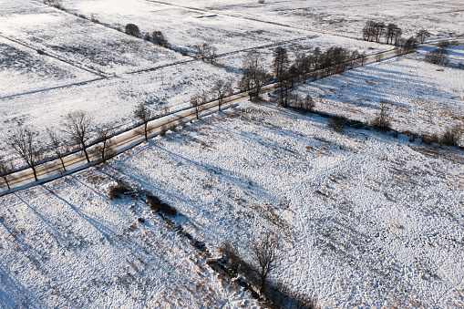 A road covered with snow among fields and meadows, view from a drone.