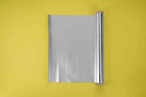Roll of aluminum foil on yellow background, top view