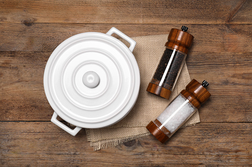 White pot with salt and pepper shakers on wooden table, flat lay