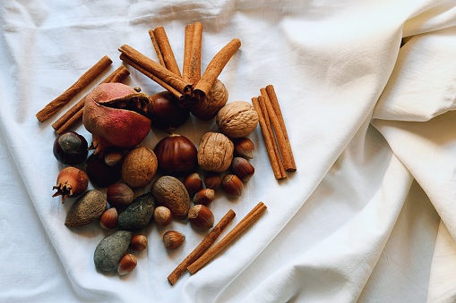 Whole and halved nutmeg seeds, cinnamon sticks, few cloves, and star anise on a white wooden background. Pumpkin spice recipe ingredients. Cooking fall dishes. Spice and seasoning concept. Front view.