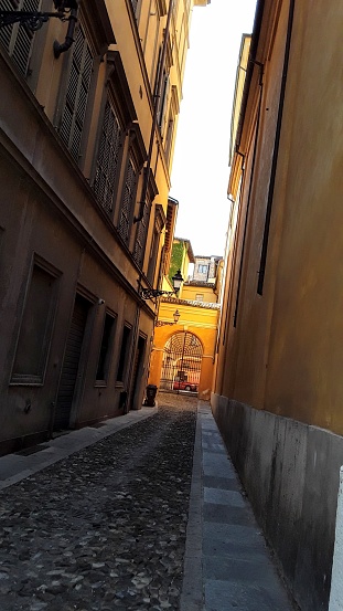 Daytime angled view of an alley in Reggio Emilia, highlighting a diminishing perspective leading to sunlight.
