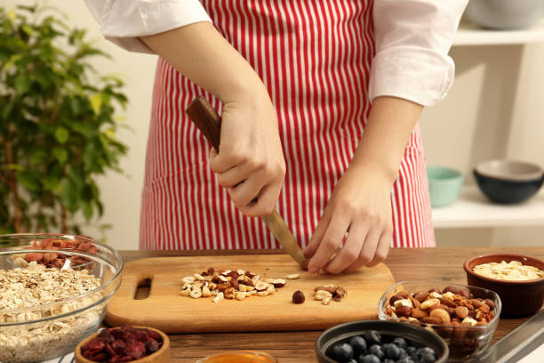 istock Making granola. Woman cutting nuts at table in kitchen, closeup 1937657378