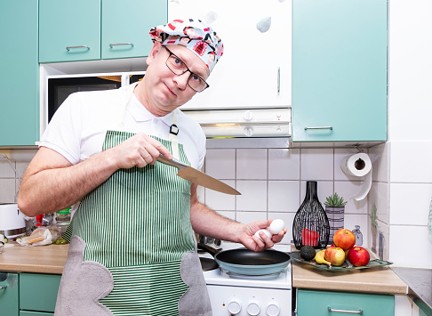 A Caucasian man, 50 years old, in a chef's hat and apron, holds chicken eggs in his hand.
