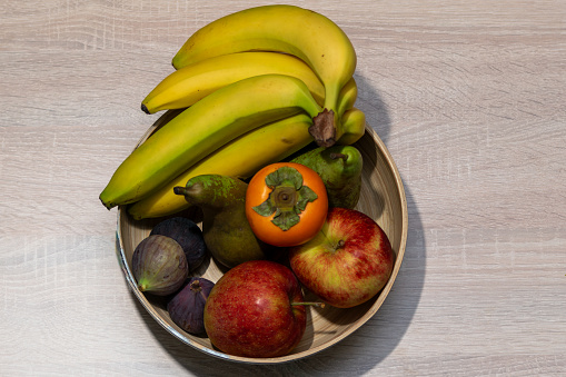 Top view of bowl containing pears apples and bananas on wood background